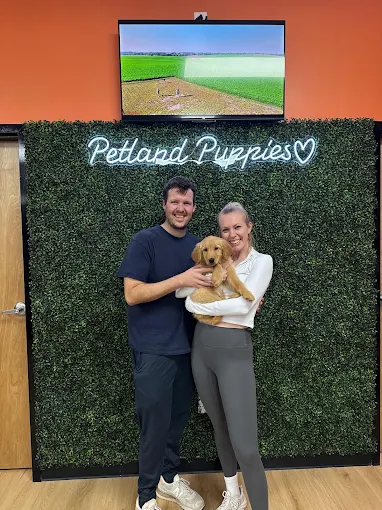 Two people holding a brown puppy inside a Petland store